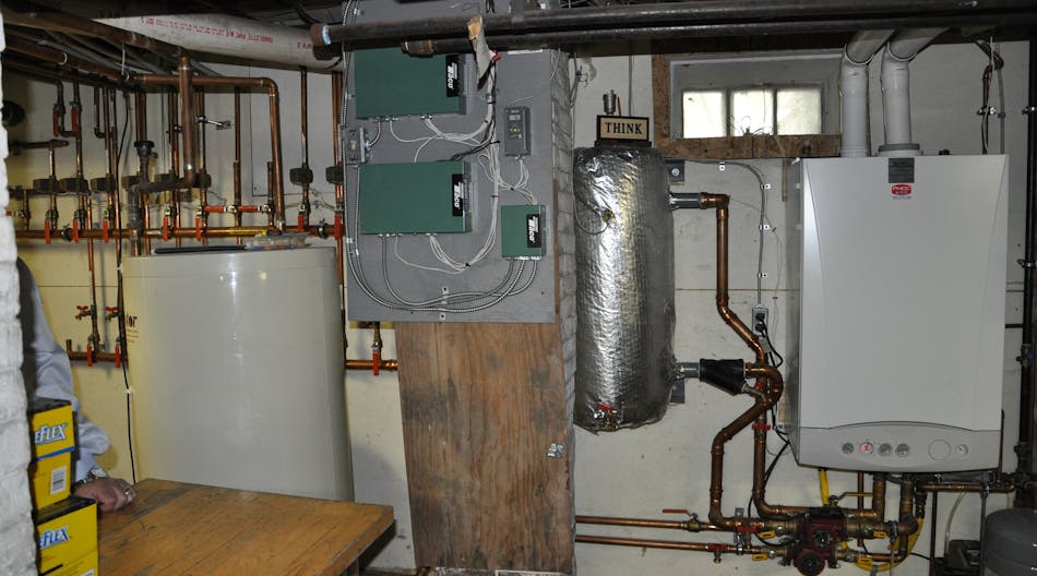 The mechanical room, with wall-hung boiler at right, thermal storage tank at left, and zone valve relays in the center.