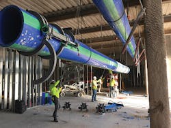 An overhead run of large-diameter Aquatherm pipe being hoisted into place. Note the prototype McElroy Acrobat&trade; 630 fusion machine&rsquo;s jaws on the pipe.