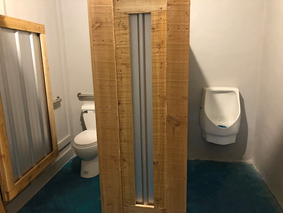 A urinal and toilet are connected to a Sanibest Pro in the men&rsquo;s restroom.