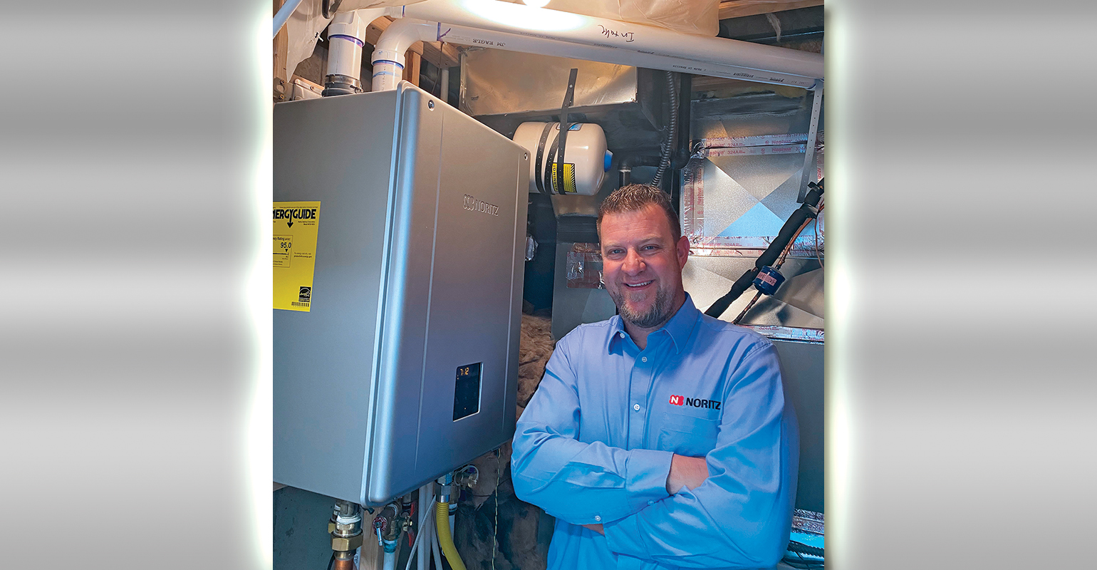 Noritz national account manager Gail Johnson inside his home&rsquo;s mechanical room with the Noritz NRCB199-DV-NG Residential Condensing Gas Combination Boiler he installed for both space heating and domestic hot water.