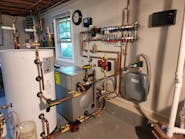 The new mechanical room. Left to right are a 42-gal. Viessmann Vito DHW tank, a Viessmann Vito Rond cast iron boiler, a Grundfos circulator and (on the wall) a Zilmet Model ZFT expansion tank. Above, on the wall, is a Viega Model 12152 Enhanced Mixing Station (with another Grundfos circulator on the left-hand side).