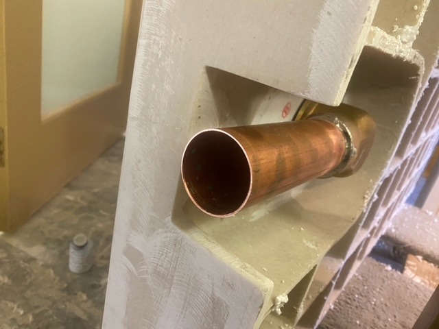 Side view of shower pan showing the side discharge shower body with brass pipe attached.