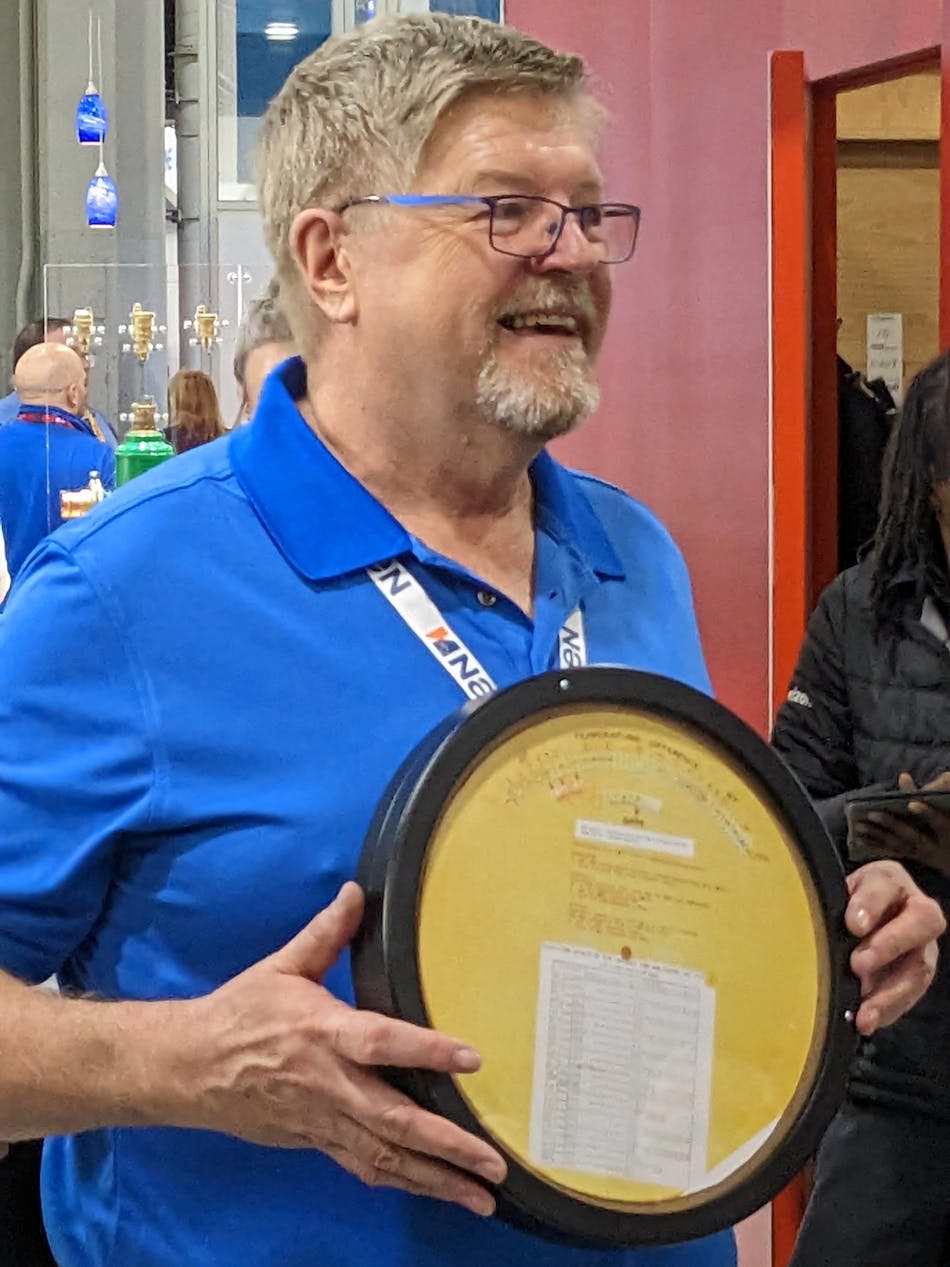 A smiling David Hughes holds his Carlson-Holohan Industry Award of Excellence&mdash;a replica of a Bell &amp; Gossett System Syzer wheel (invented by Carlson).