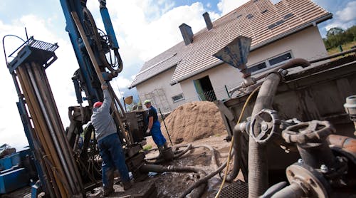 Two workmen drilling a residential geothermal field.