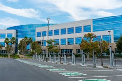 A row of electric vehicle charging stations with dedicated parking spots stands at outdoor parking lot of commercial office building. A row of electric vehicle charging stations with dedicated parking spots stands at outdoor parking lot of commercial office building.
