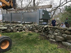 The bobcat carefully lifting the fluid cooler over an ancient stone wall.