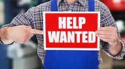 Male Technician Pointing At Help Wanted Sign