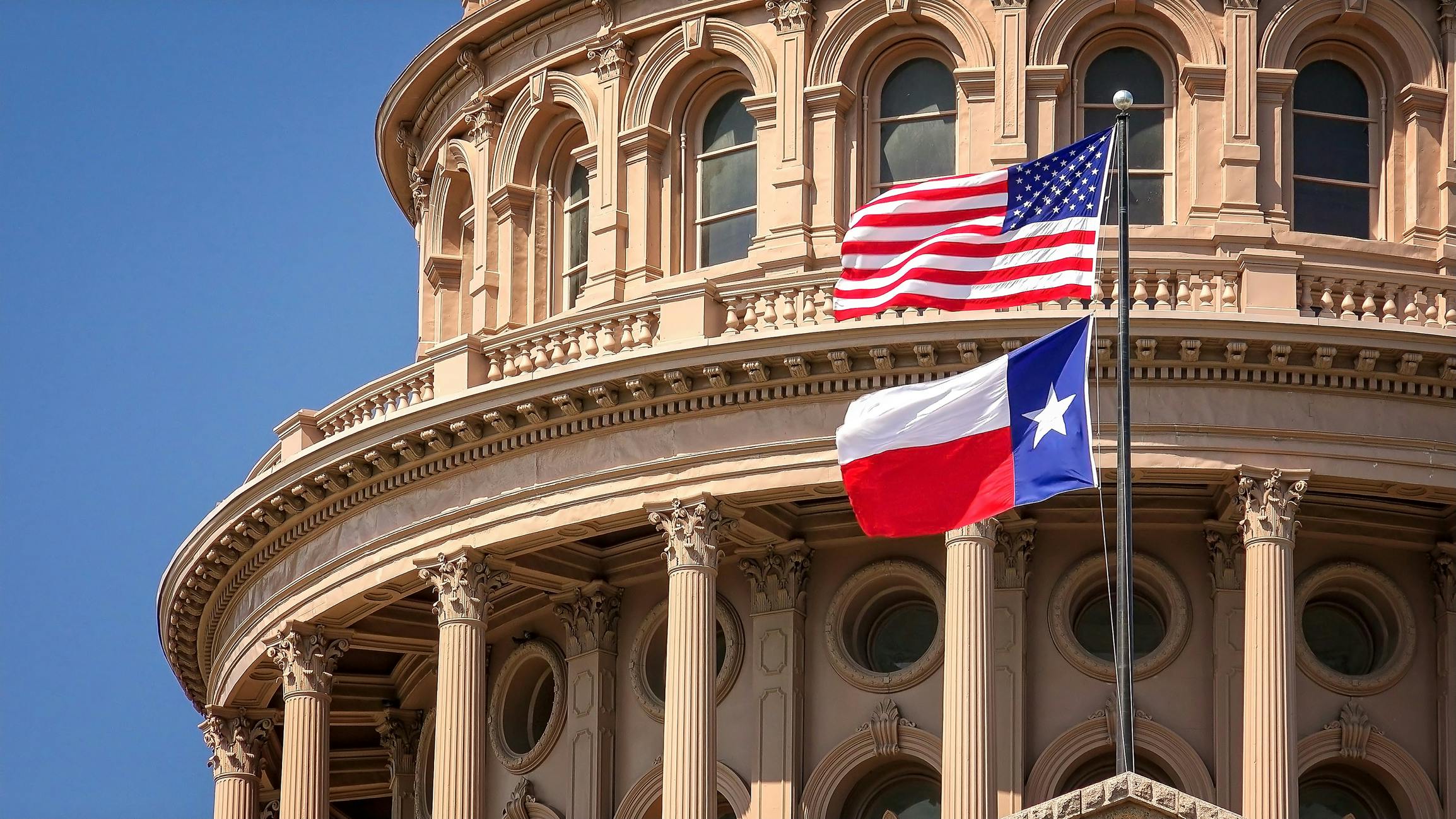 American and Texas state flags flying on the dome of the Texas State Capitol building in Austin.