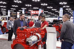An exhibitor engages with two attendees at a booth in exhibit hall. An exhibitor engages with two attendees at a booth in exhibit hall.