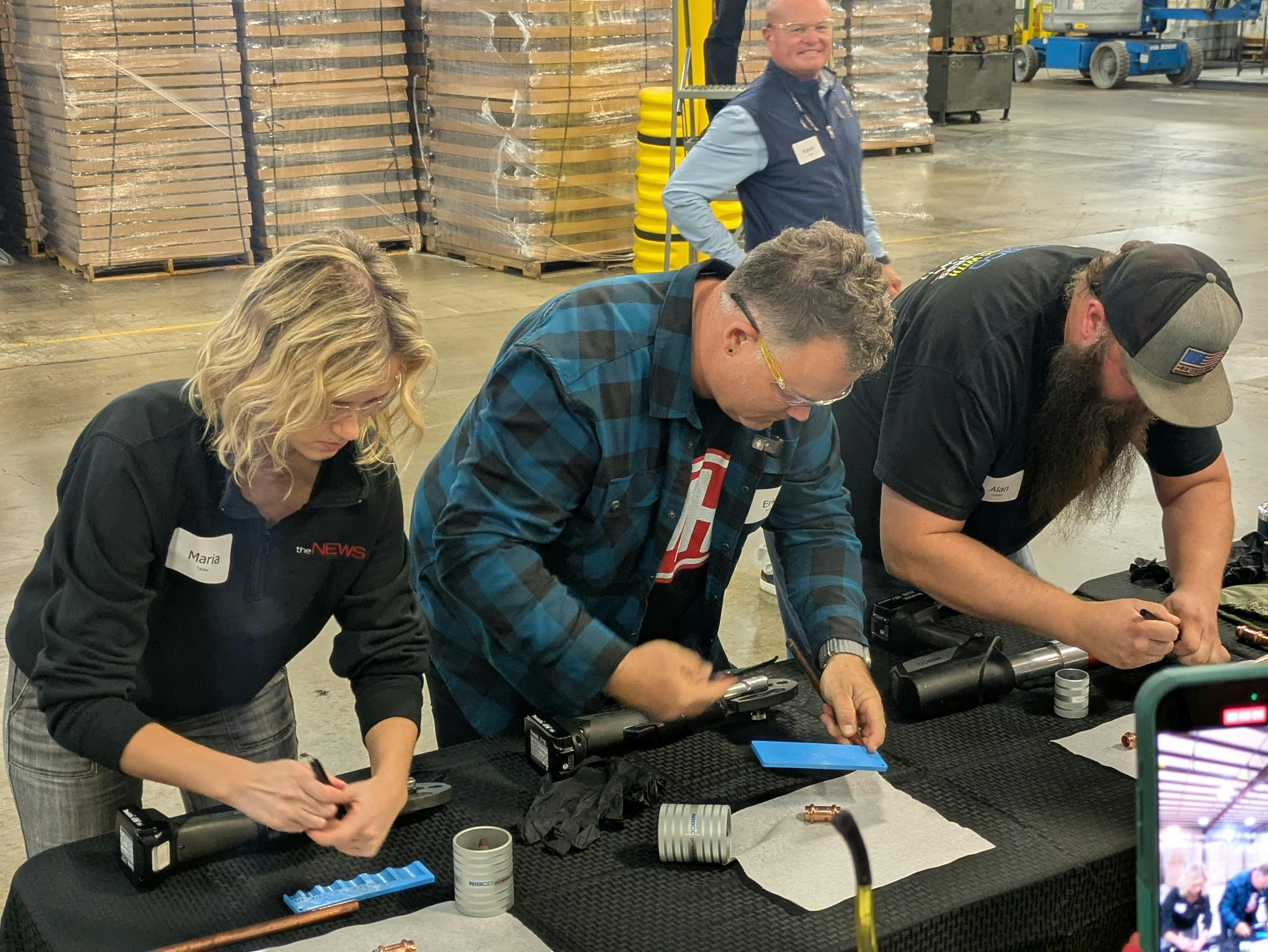 Maria Taylor (ACHR NEWS), Eric Aune (Mechanical Hub) and victorious Alan 'Coach' Carlson (Armbrust Plumbing) compete in a fitting pressing competition.