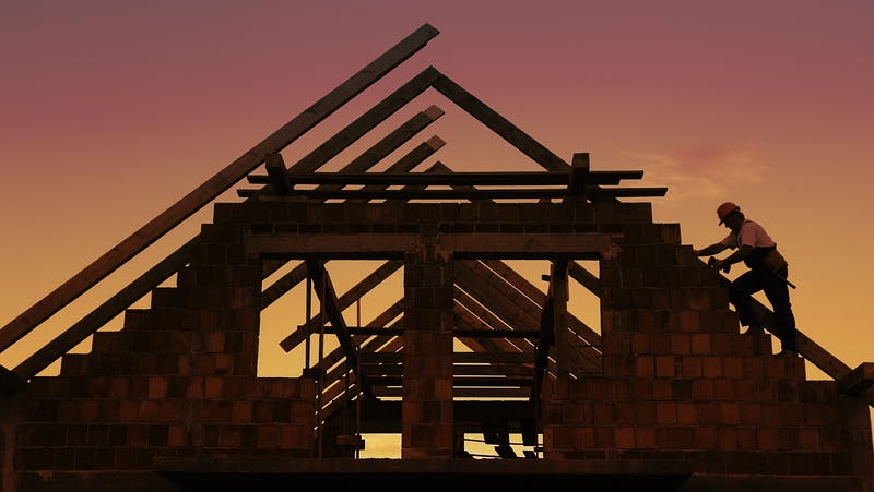 Construction worker working with house wooden roof against sunset sky