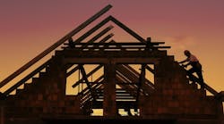 Construction worker working with house wooden roof against sunset sky Construction worker working with house wooden roof against sunset sky