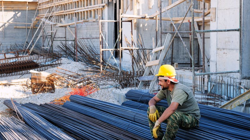 Construction worker resting on steel bars.
