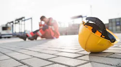 Yellow hardhat at shipyard with depressed male worker in background Yellow hardhat at shipyard with depressed male worker in background