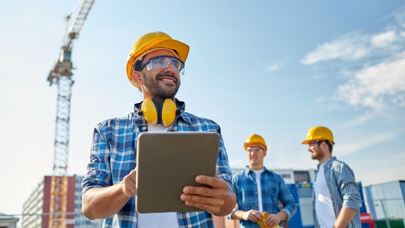 Builder in hardhat with tablet pc at construction site.