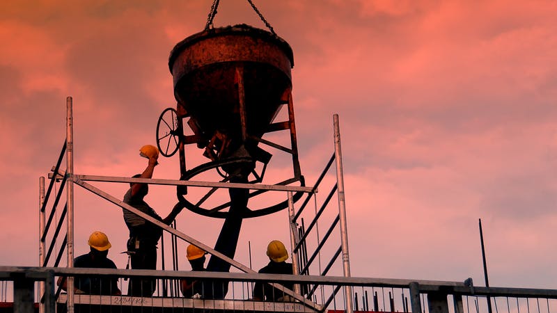 Silhouettes of construction workers pouring concrete mix at the building site