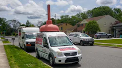 Front of a white plumbing company truck that has a huge plunger on its roof. Front of a white plumbing company truck that has a huge plunger on its roof.