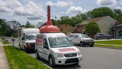 Front of a white plumbing company truck that has a huge plunger on its roof. Front of a white plumbing company truck that has a huge plunger on its roof.