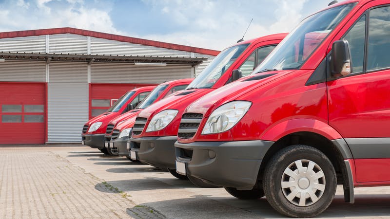 Row of red delivery and service cars in front of a factory and warehouse distribution plant
