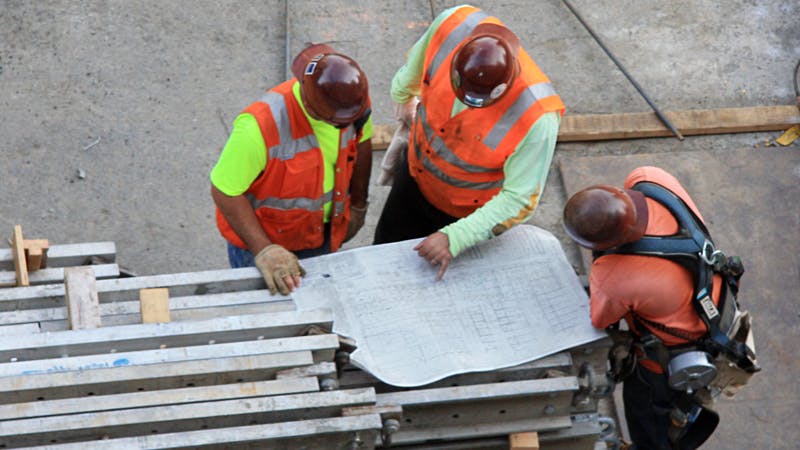 Three construction workers looking at construction drawing blueprint