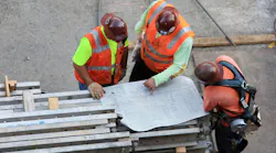 Three construction workers looking at construction drawing blueprint