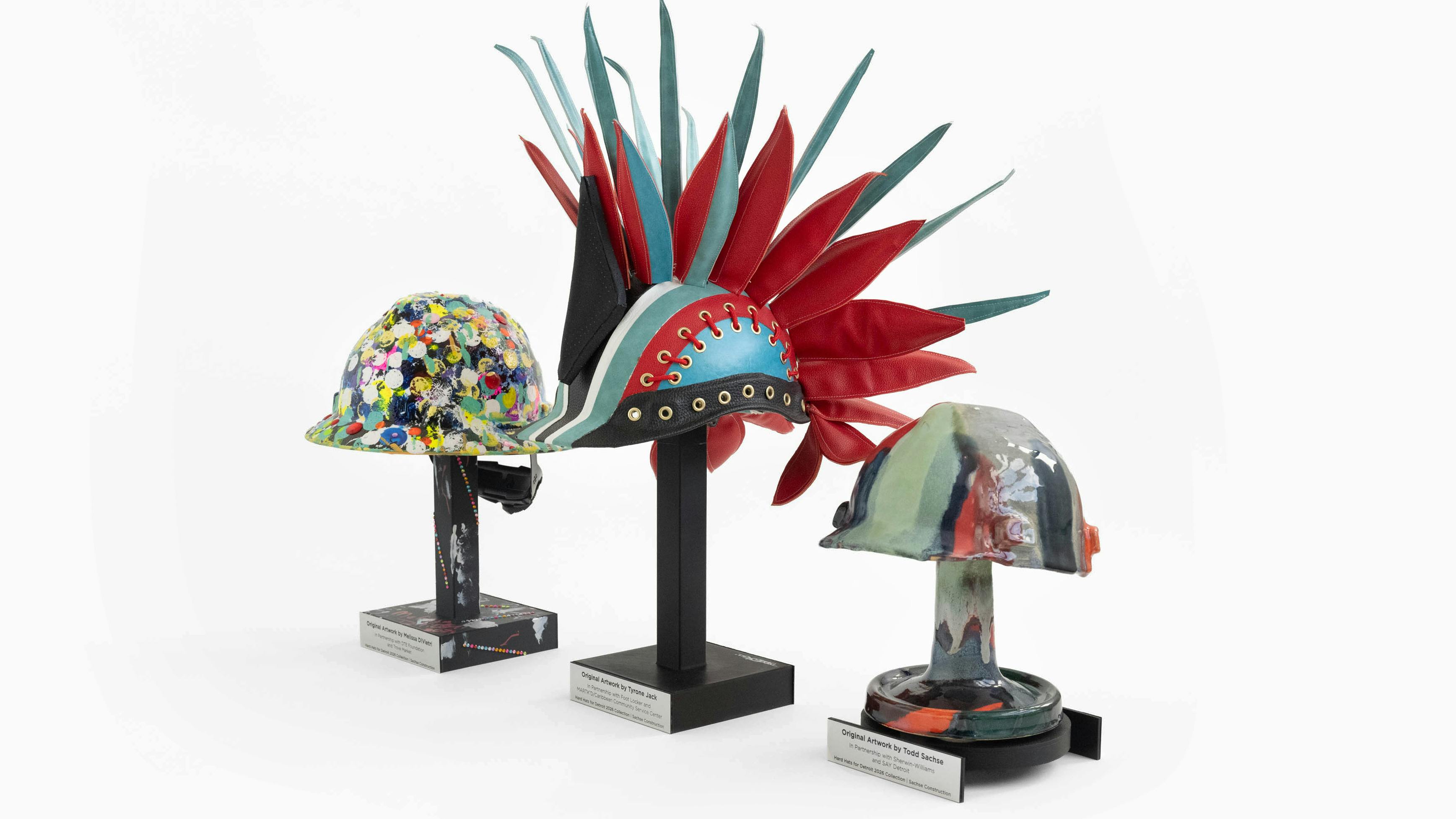Three hard hats created by artist and disability advocate Melissa DiVietri, General Motors automotive design modeler and oil painter Tyrone Jack, and Sachse Construction CEO Todd Sachse.